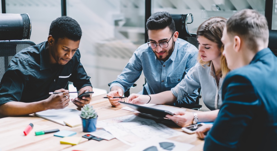 Group of diversity people searching information for provide ideas in new startup project using touch pad during brainstorming, collaboration and cooperation. Four colleagues sharing opinions at meeting